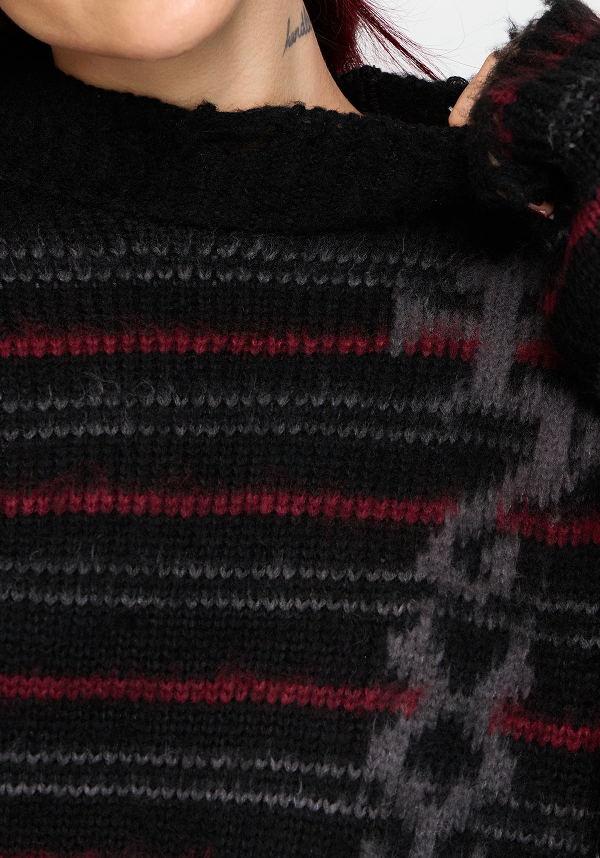 Close-up of a person wearing a chunky knit sweater with a black base and horizontal red and gray stripes.