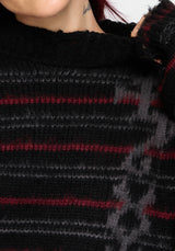 Close-up of a person wearing a chunky knit sweater with a black base and horizontal red and gray stripes.