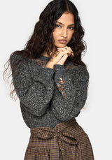 A woman modeling a dark gray marled knit sweater with distressed details and brown lace-up plaid skirt against a light gray background.