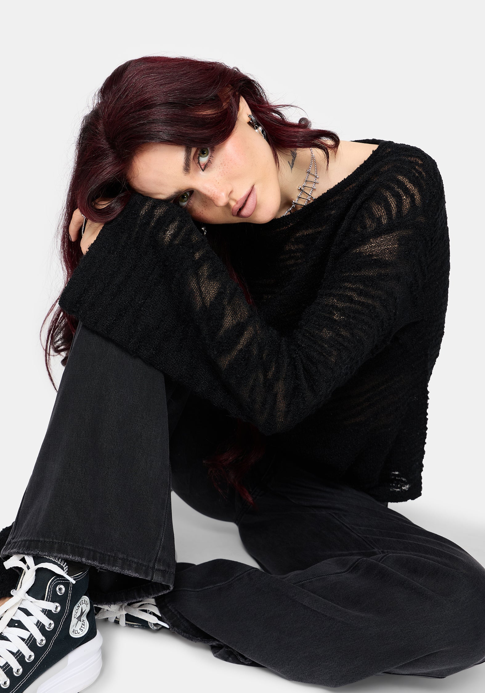 Woman wearing a black distressed jumper with long sleeves and back denim jeans on a white background