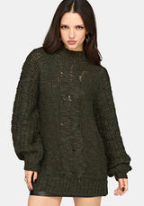A woman modeling a dark olive green chunky knit sweater with distressed details, photographed against a light gray studio background.