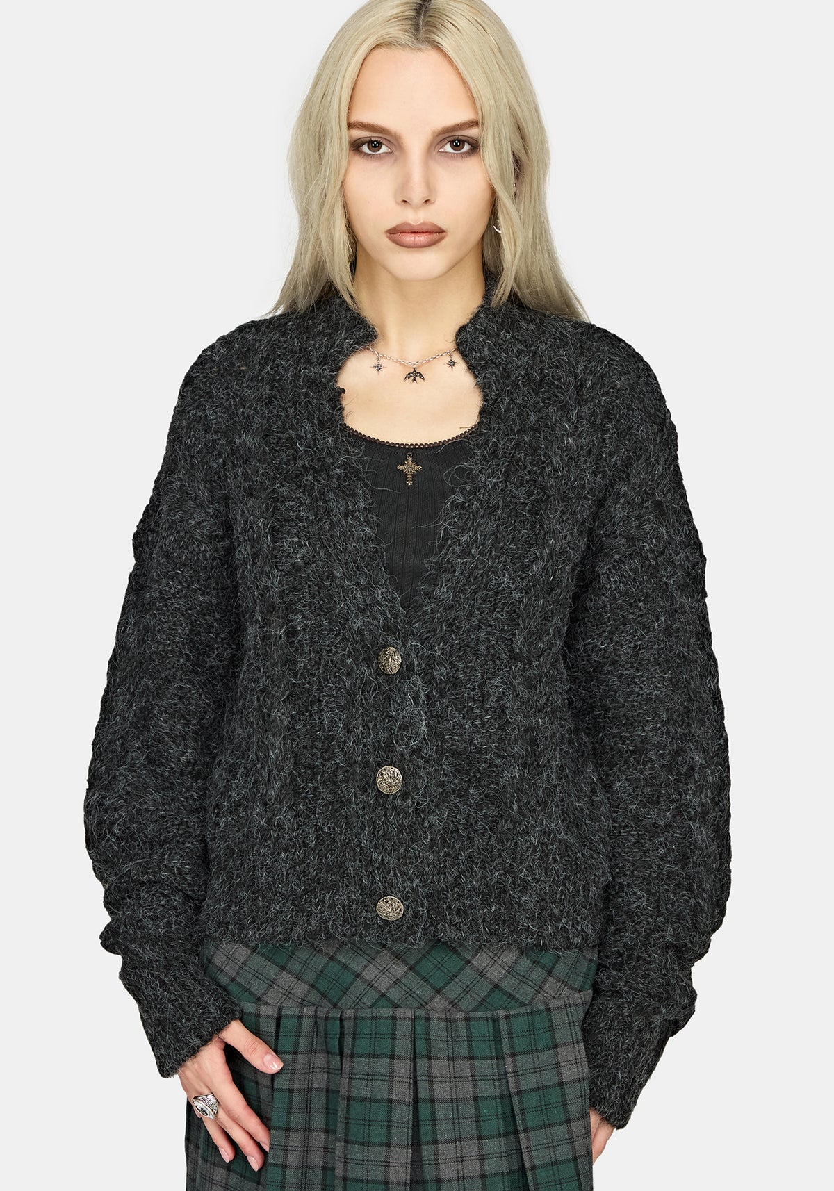 A model wearing a dark gray marled textured cardigan over a black top and a green plaid skirt, photographed against a light gray background.
