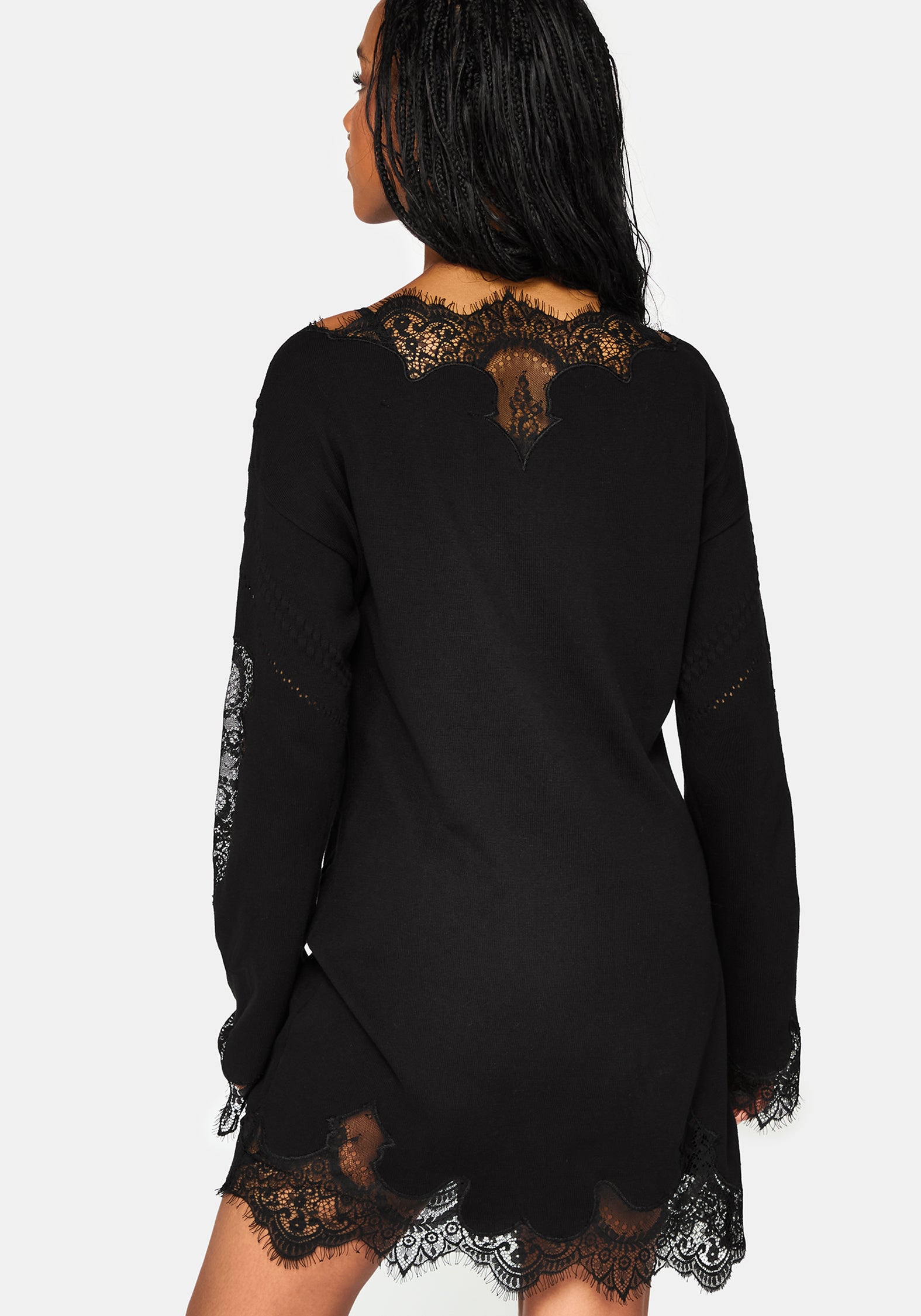 A woman shown from the back wearing a black long-sleeve mini dress with lace trim at the neckline, sleeves, and hem, against a light gray studio background.