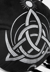 A circular black cushion with a white Celtic knot triquetra design, a small sun motif at the top, and tassels extending from the outer edge, shown on a light gray background.
