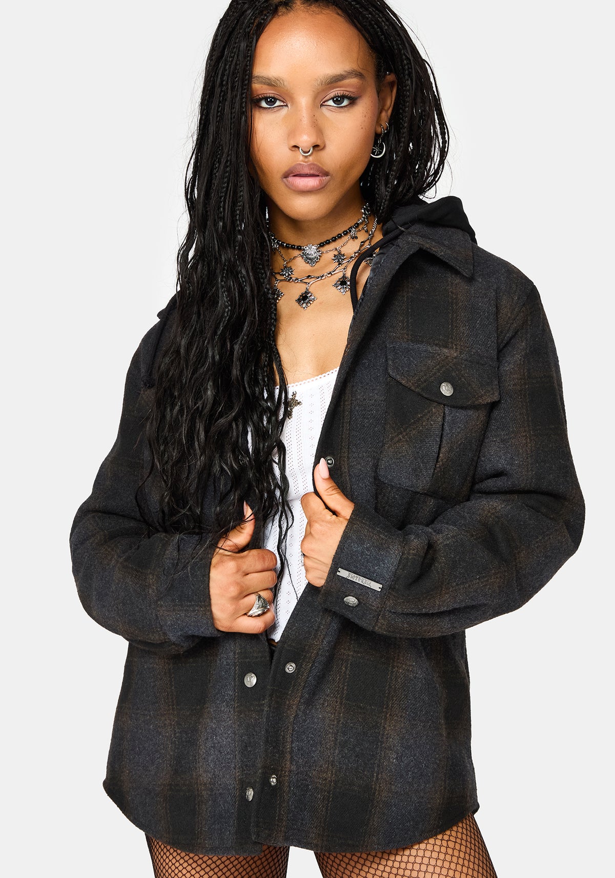 A woman modeling a dark charcoal gray and black plaid hooded button-up shirt jacket over a white top, set against a plain light gray studio background.