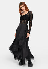 A model wearing a long black lace and mesh maxi dress with a high-low layered skirt and black platform boots, photographed against a light gray studio background.