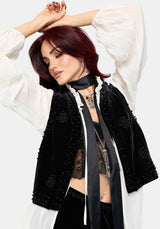 A model with dark red hair wearing a black velvet embroidered vest over a white long-sleeve blouse, styled with a black ribbon and lace.