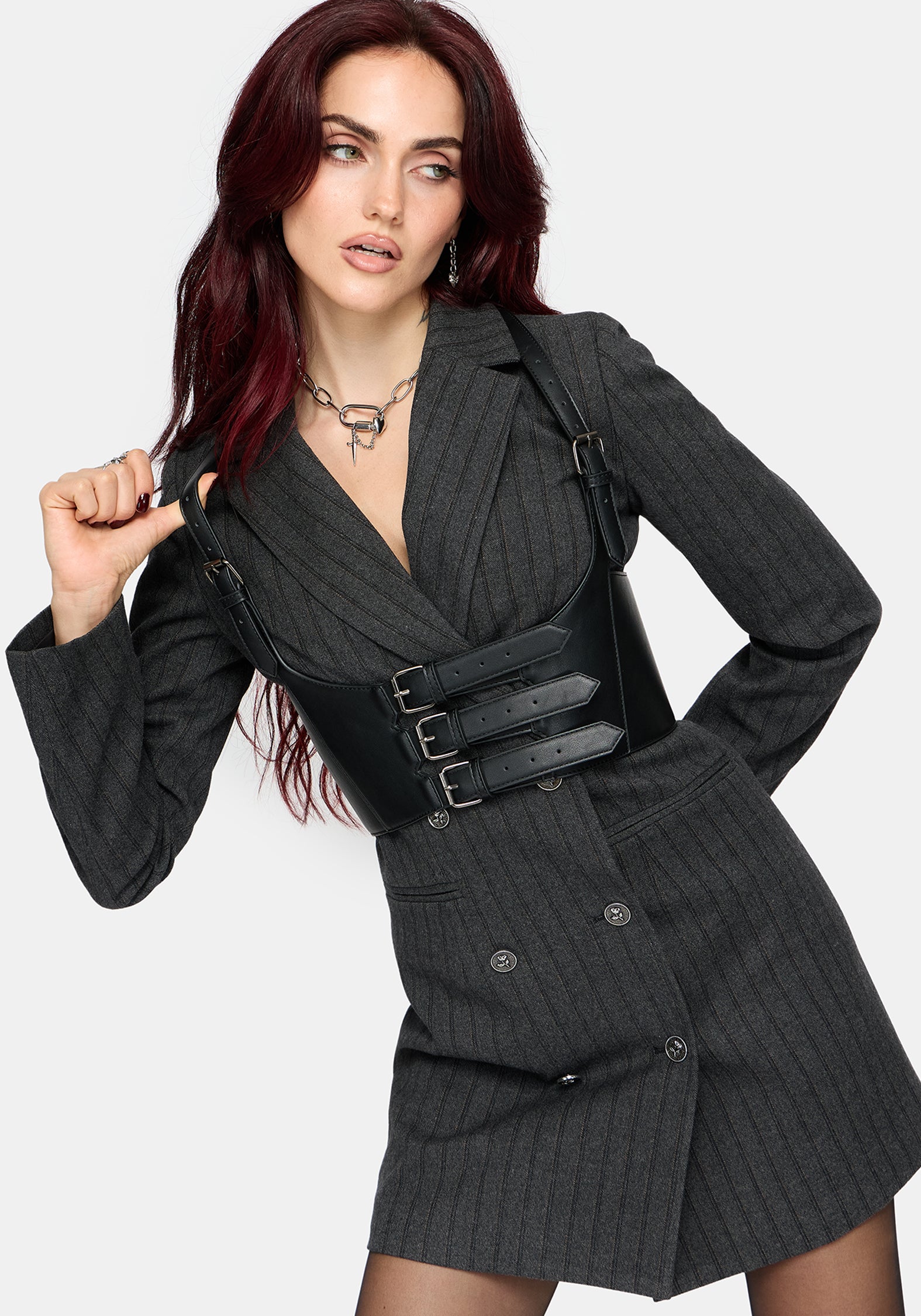 A model with dark red hair wearing a dark gray pinstriped double-breasted blazer and matching mini skirt, styled with a wide black faux-leather belt featuring silver buckles.