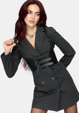 A model with dark red hair wearing a dark gray pinstriped double-breasted blazer and matching mini skirt, styled with a wide black faux-leather belt featuring silver buckles.