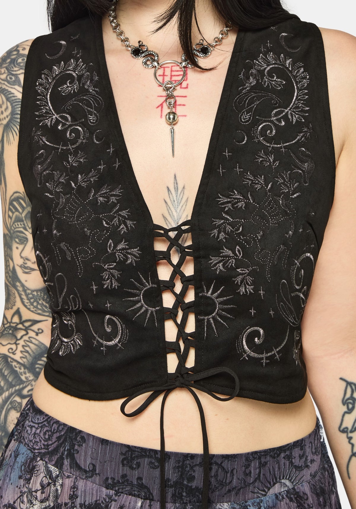 Woman wearing a black lace-up top with intricate designs on a plain background