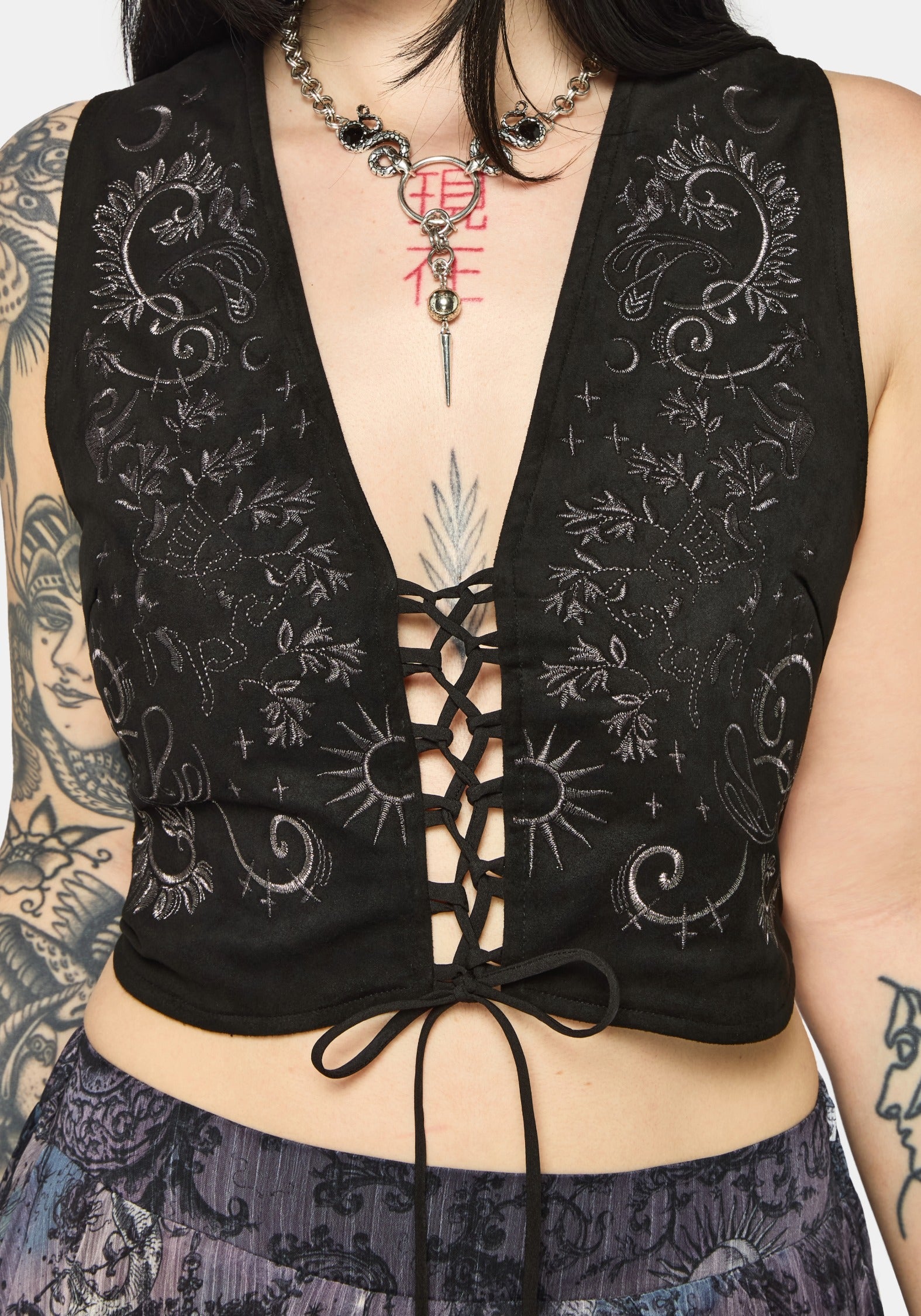 Woman wearing a black lace-up top with intricate designs on a plain background