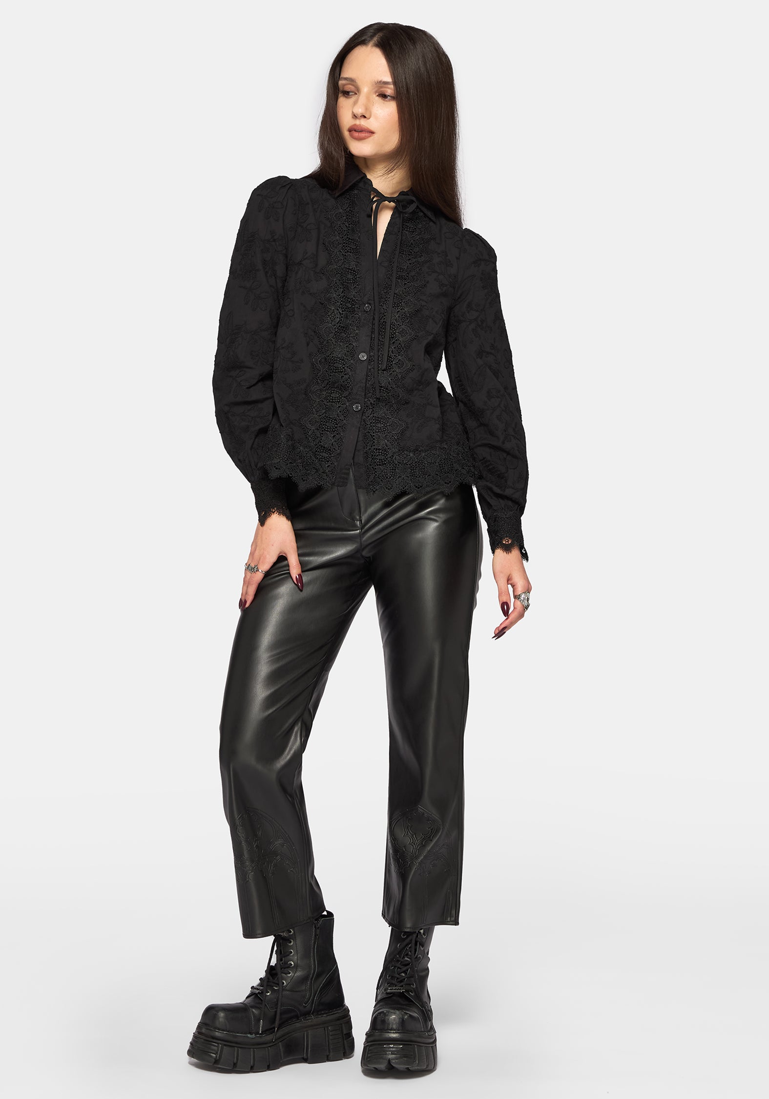 Woman wearing a black long sleeve lace detail blouse with black leather pants on a plain background