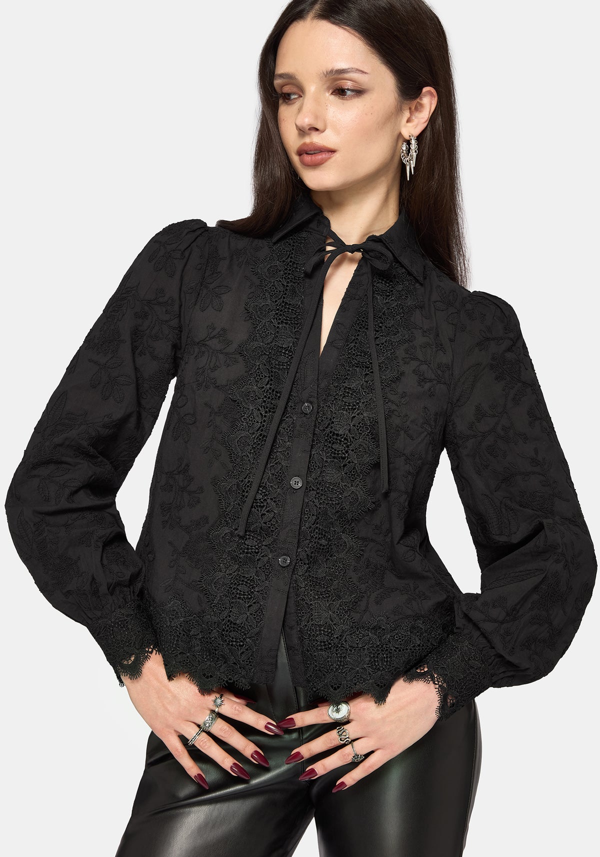Woman wearing a black long sleeve lace detail blouse with a plain background