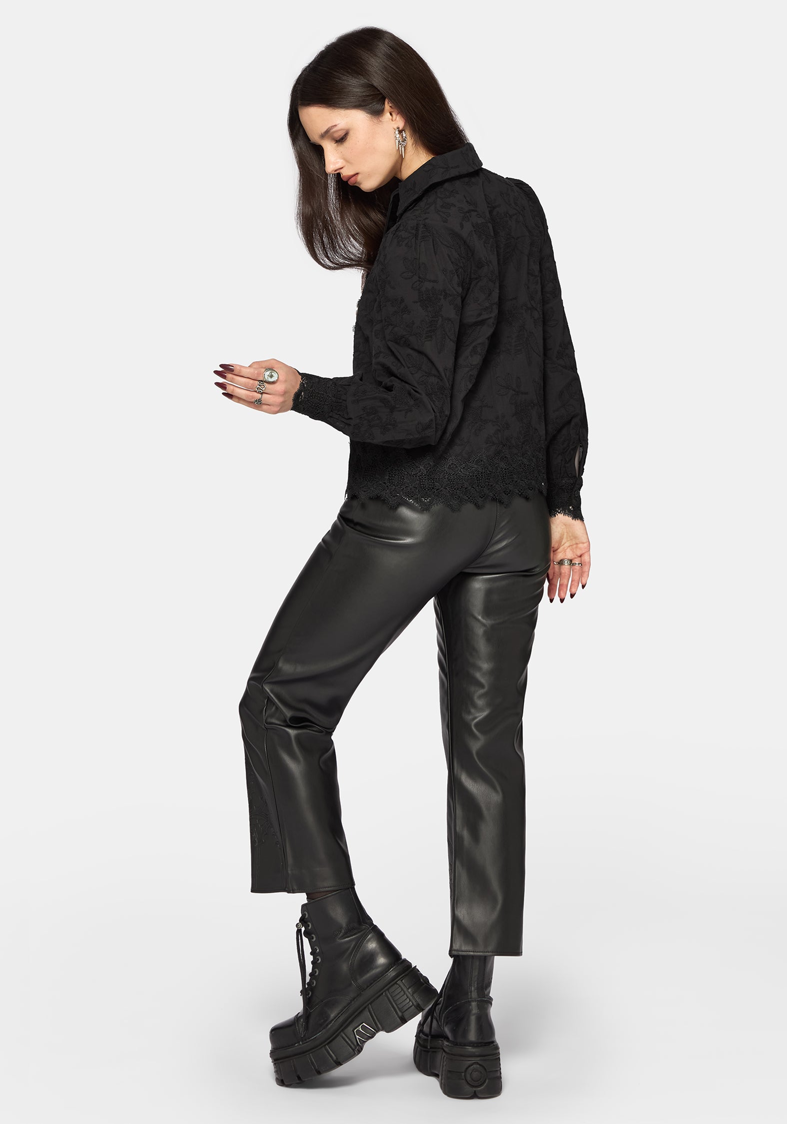 Woman wearing a black long sleeve blouse with leather pants on a white background