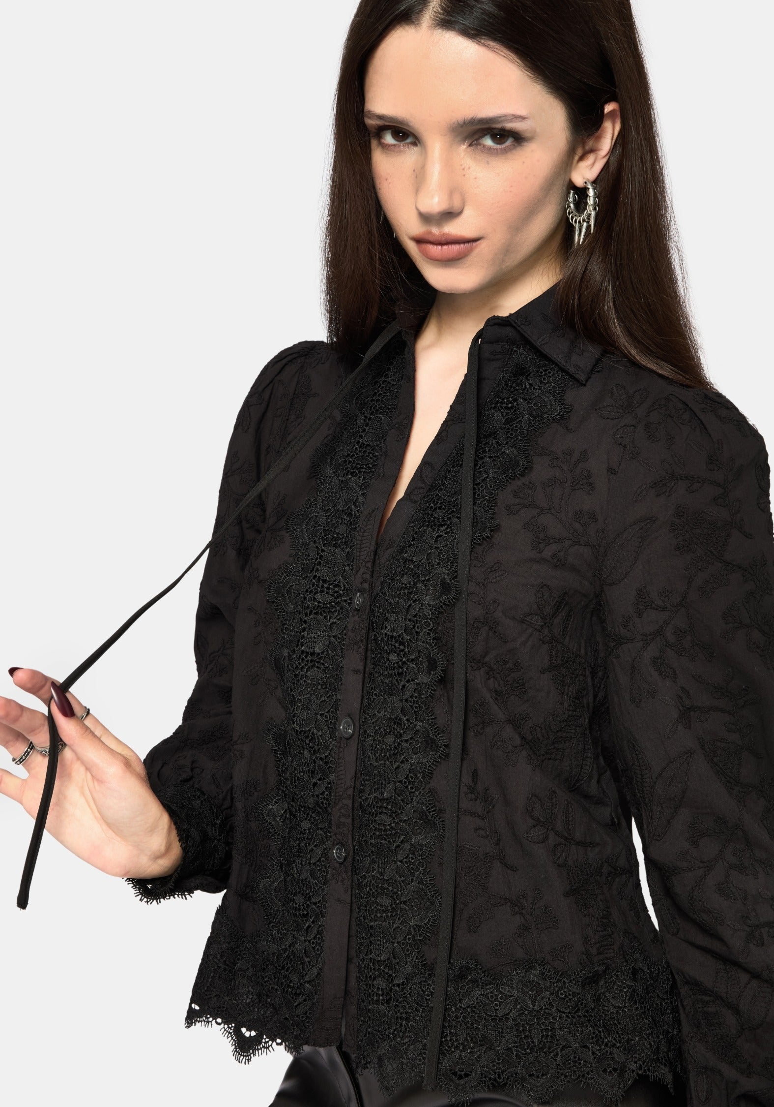 Woman wearing a black lace detail blouse against a white background