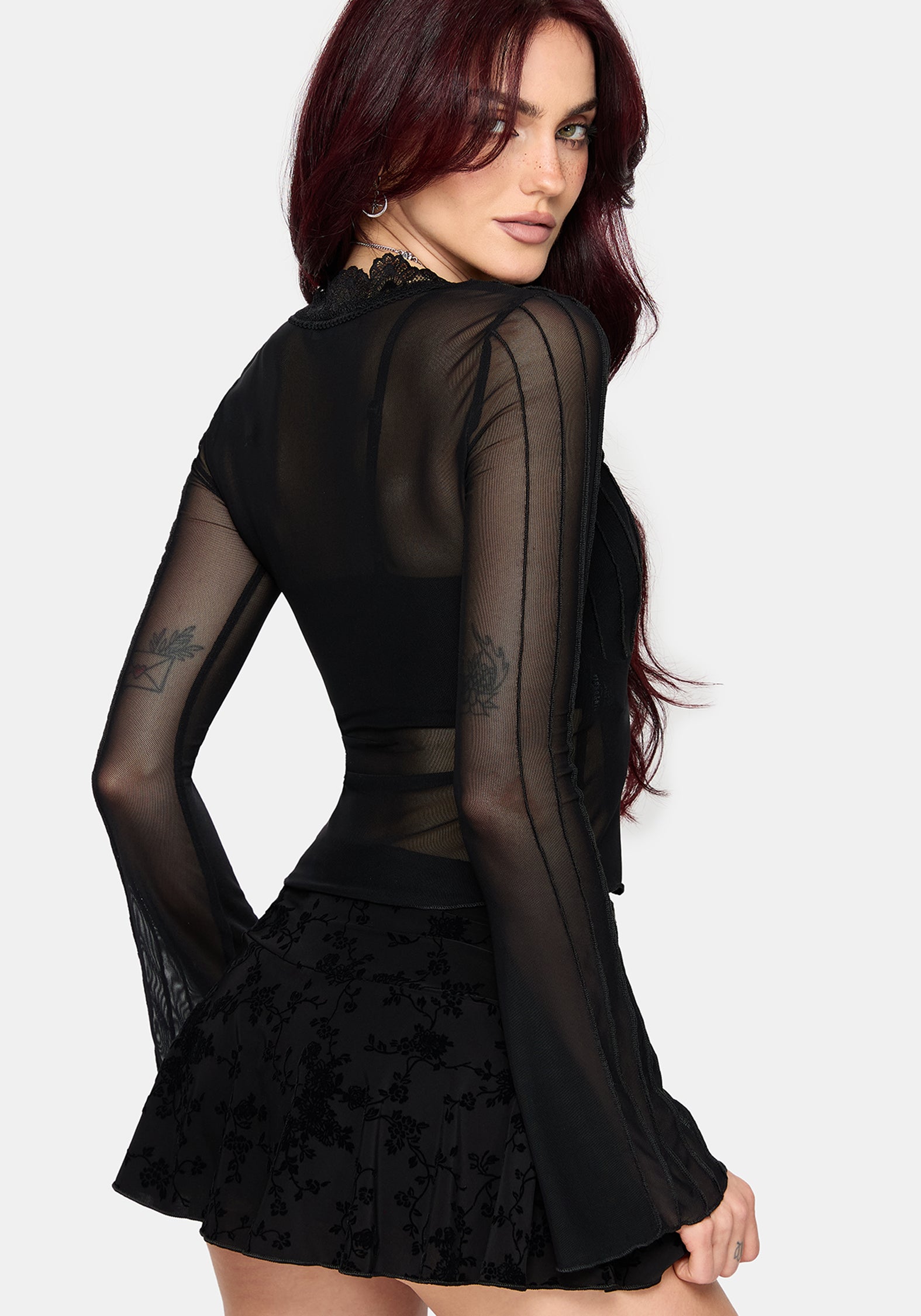 Woman wearing a black lace mesh top with long sleeves on a plain background