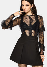 Woman wearing a black lace top and black mini skirt on a white studio background.