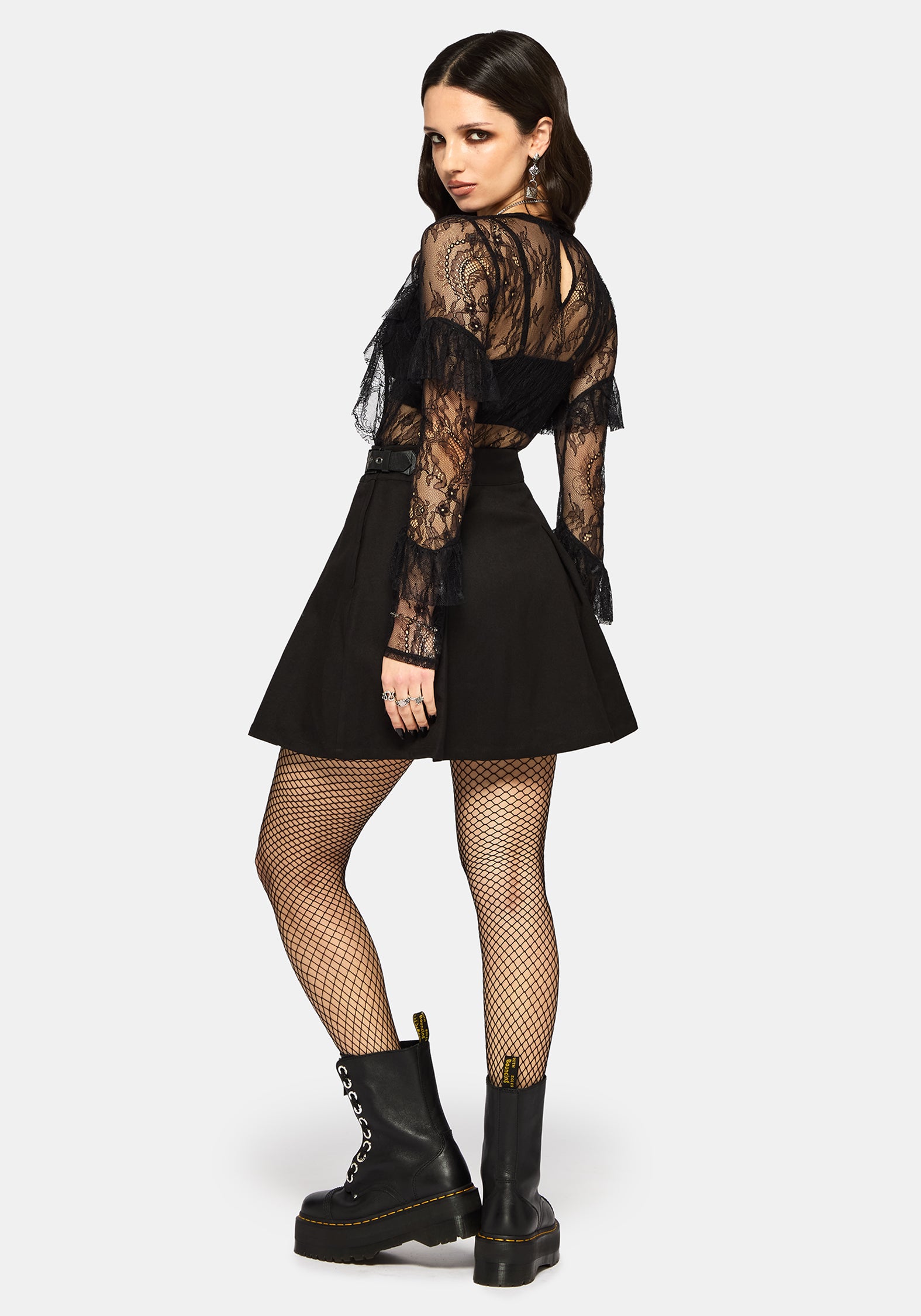 Woman wearing a black lace top, black skirt, and black boots on a white studio background