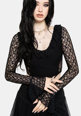 A woman modeling a black long-sleeve lace top with a ruffled scoop neckline and sheer lace sleeves, paired with a black skirt, against a light gray studio background.