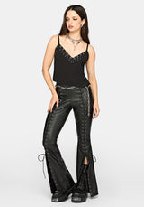 A model wearing a black studded camisole top and black faux-leather flared pants with lace-up details and side chain accents, styled with black platform boots against a light gray studio background.