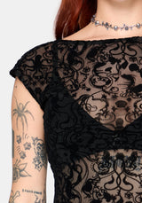 Black lace top worn by a person with tattoos on their arm.