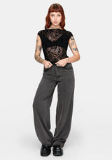Woman wearing a sheer black lace top and gray straight leg jeans on a white background