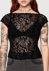 Person wearing a sheer black lace top with tattoos visible on arms and neck.