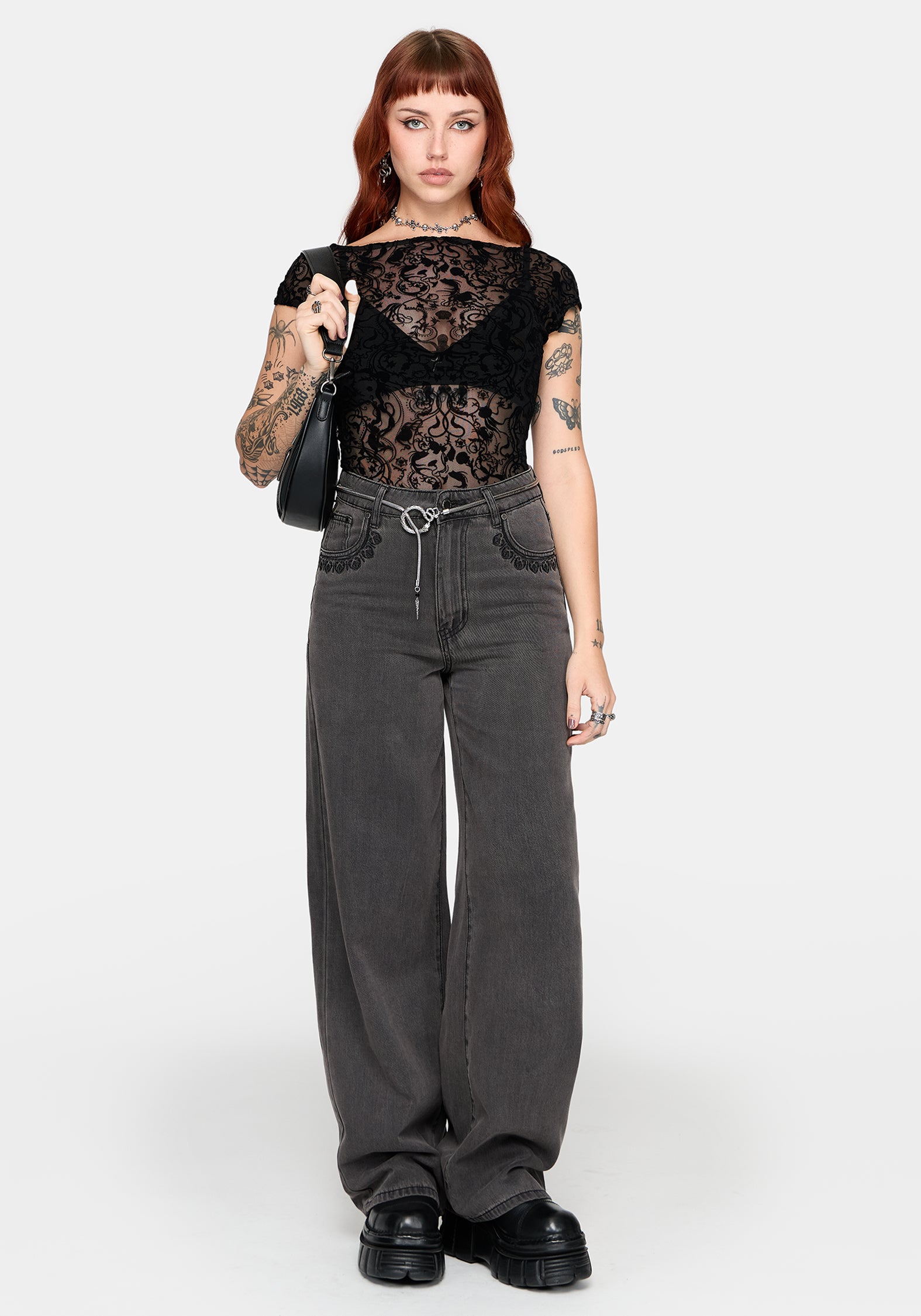 Woman wearing a black lace top and gray straight leg jeans on a white background