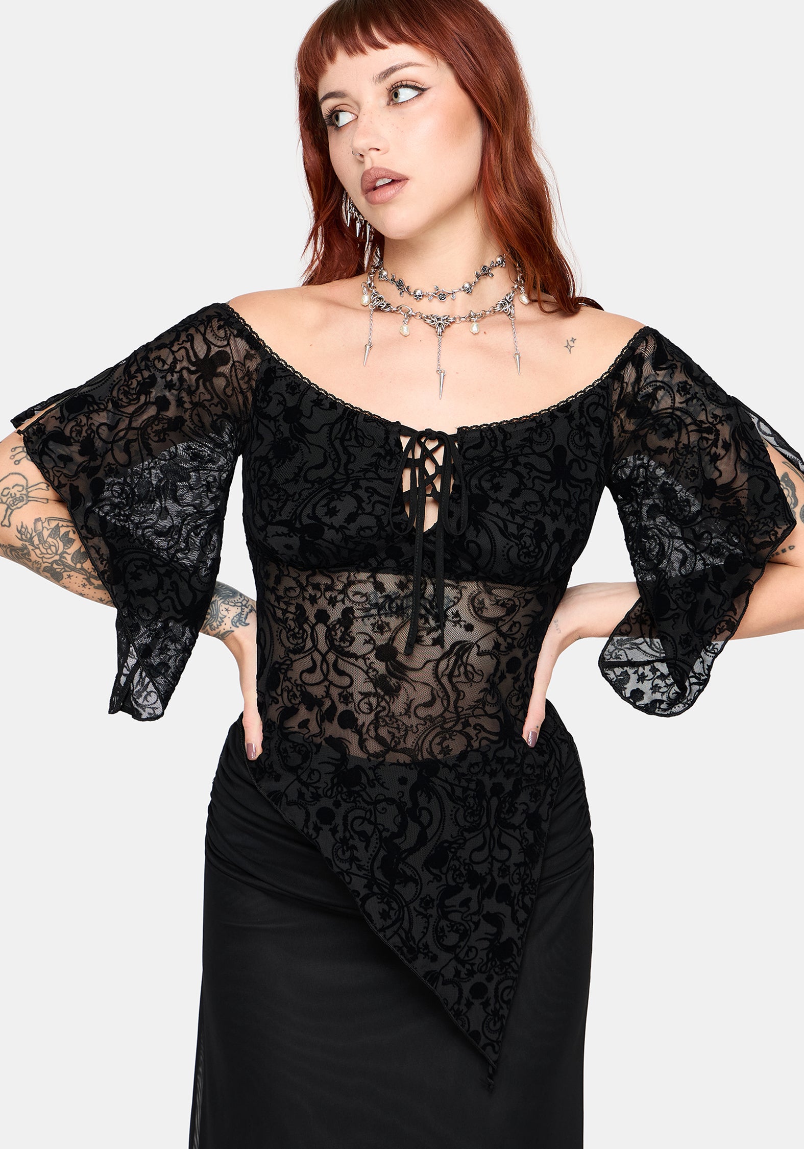 Woman wearing a black lace top with flared 3/4 sleeves and sheer panels on a white background