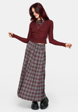A woman wearing a ribbed long-sleeve button-front knit top in deep burgundy, paired with a gray and burgundy plaid skirt and layered silver chain necklaces, against a light gray studio background.
