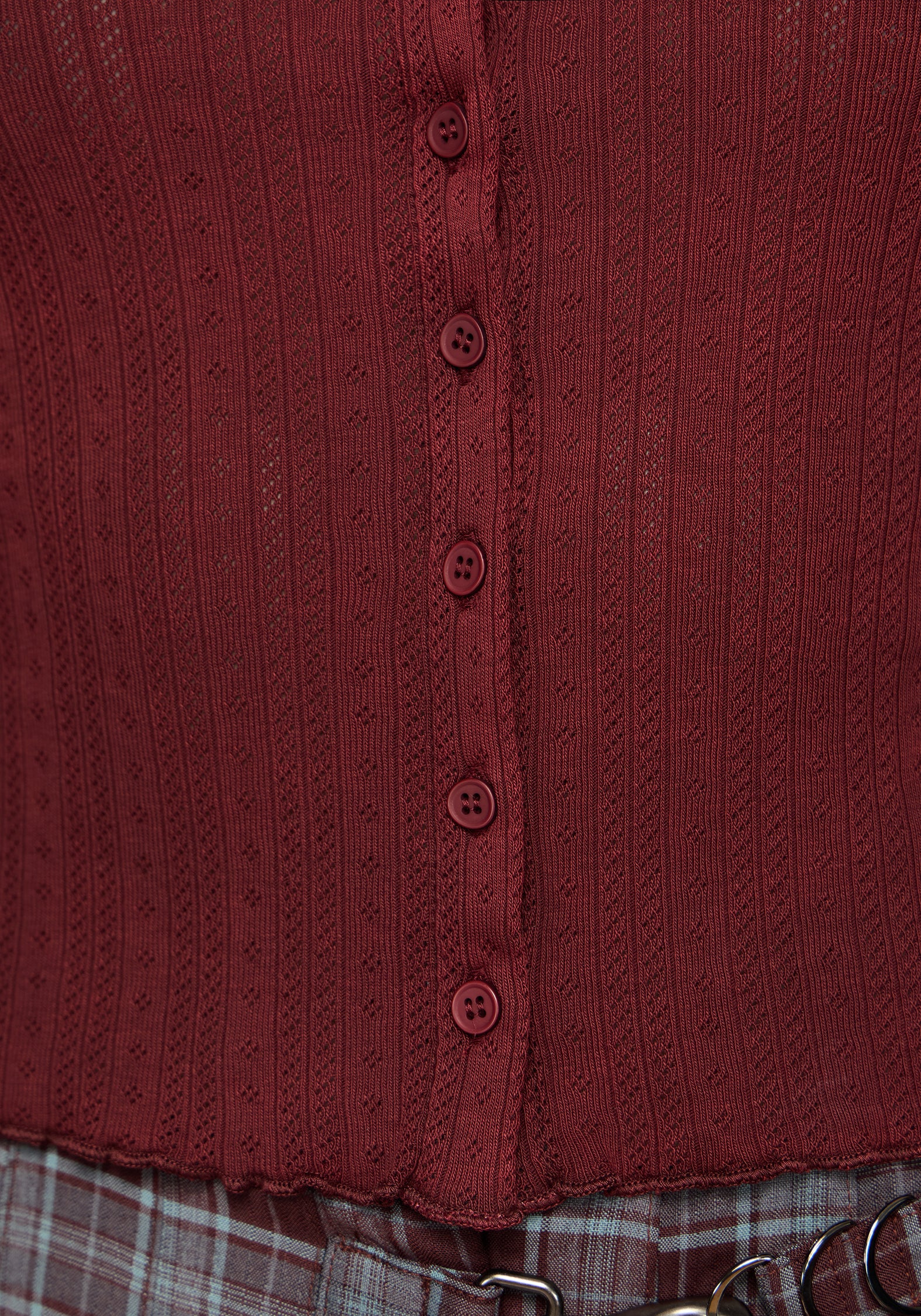 Close-up of a ribbed knit top in a deep burgundy red, featuring a vertical button placket with matching buttons and a ruffled hem.