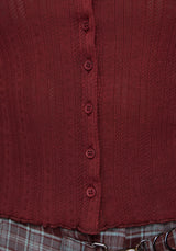 Close-up of a ribbed knit top in a deep burgundy red, featuring a vertical button placket with matching buttons and a ruffled hem.