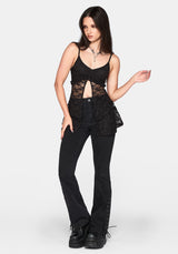 A woman modeling a black lace cutout camisole top and black high-waisted flare jeans with lace-up details down the sides, paired with black platform shoes, against a light gray studio background.