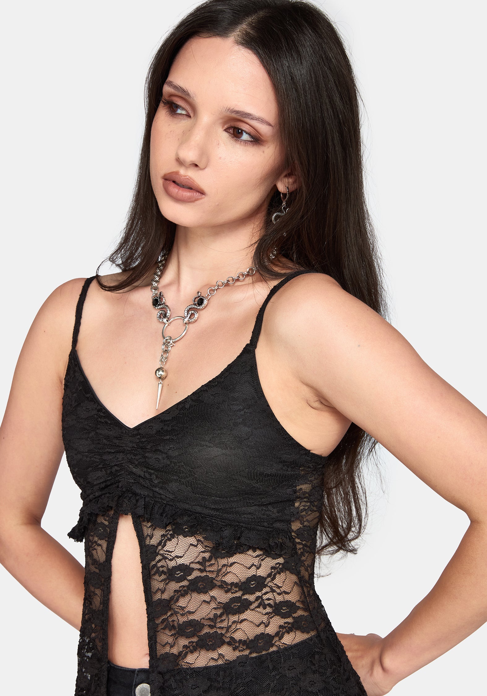 A woman wearing a black lace camisole top with thin straps, a ruched sweetheart neckline, and a side slit, paired with silver statement jewelry against a light gray background.